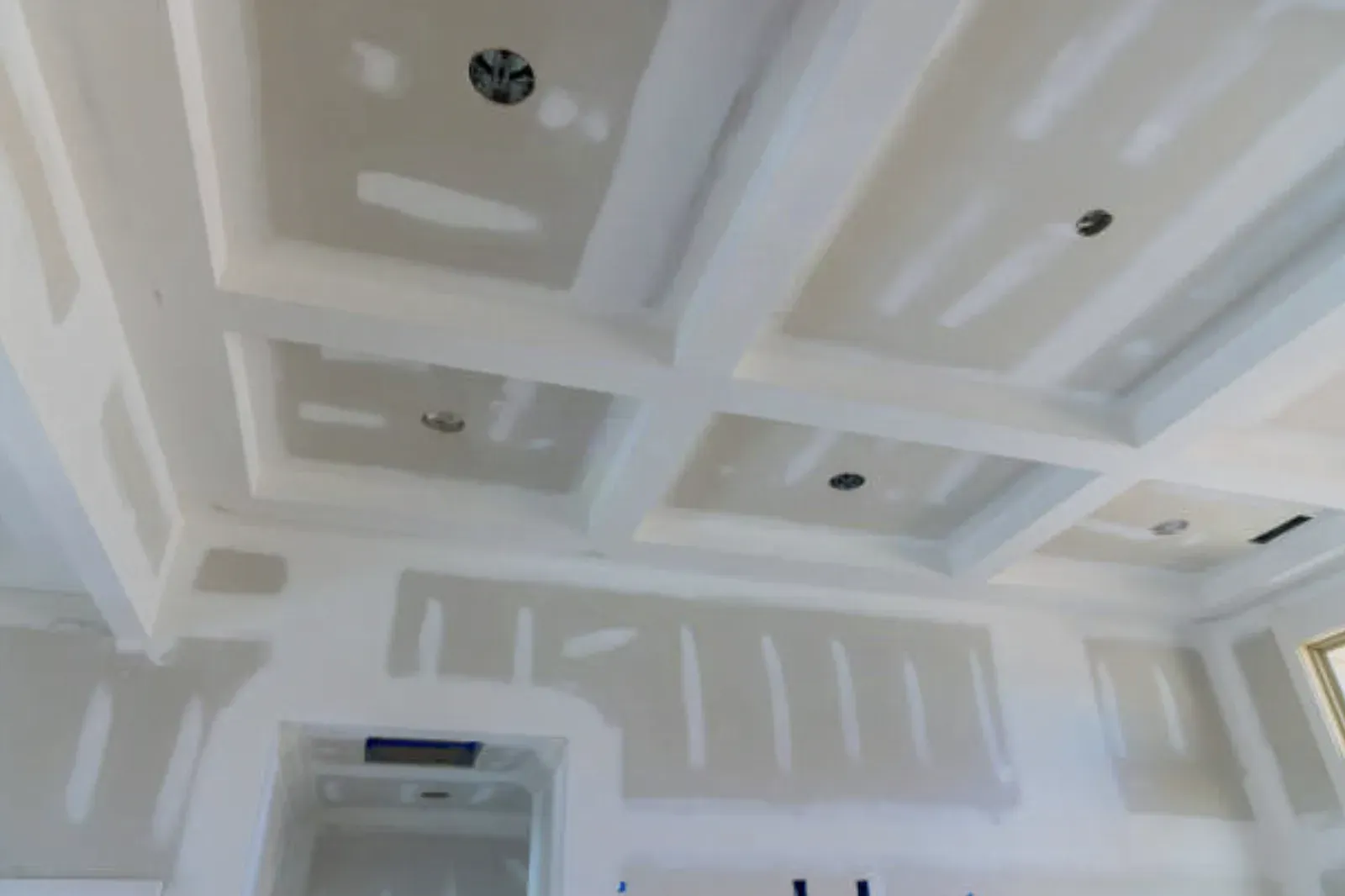 Coffered drywall ceiling with recessed lights, beam corners and flat-panel seams taped and coated, walls spotted with joint compound