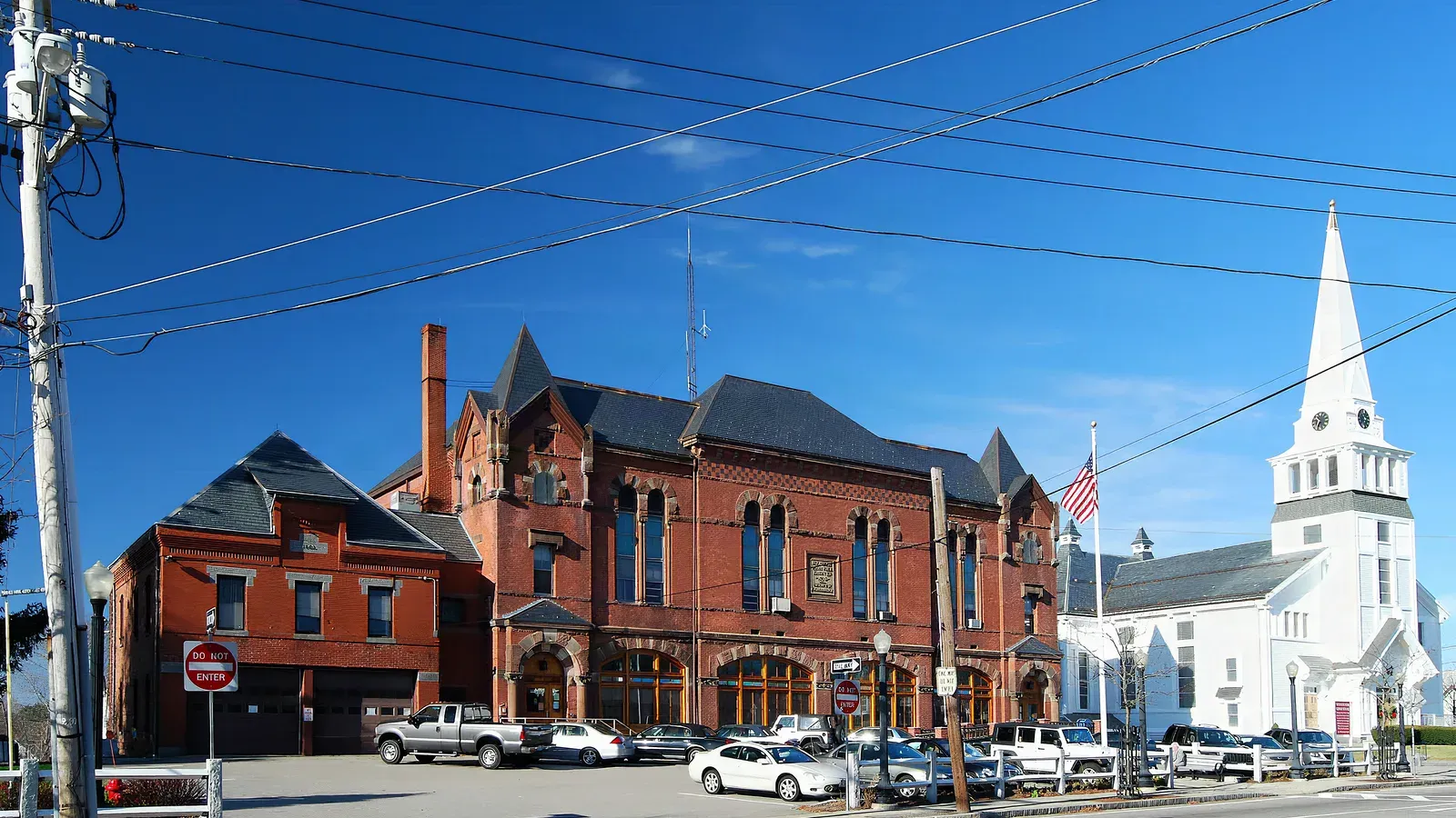 Holbrook Town Hall, a Victorian red-brick civic building beside a white-steepled church in the town center, Holbrook, Massachusetts