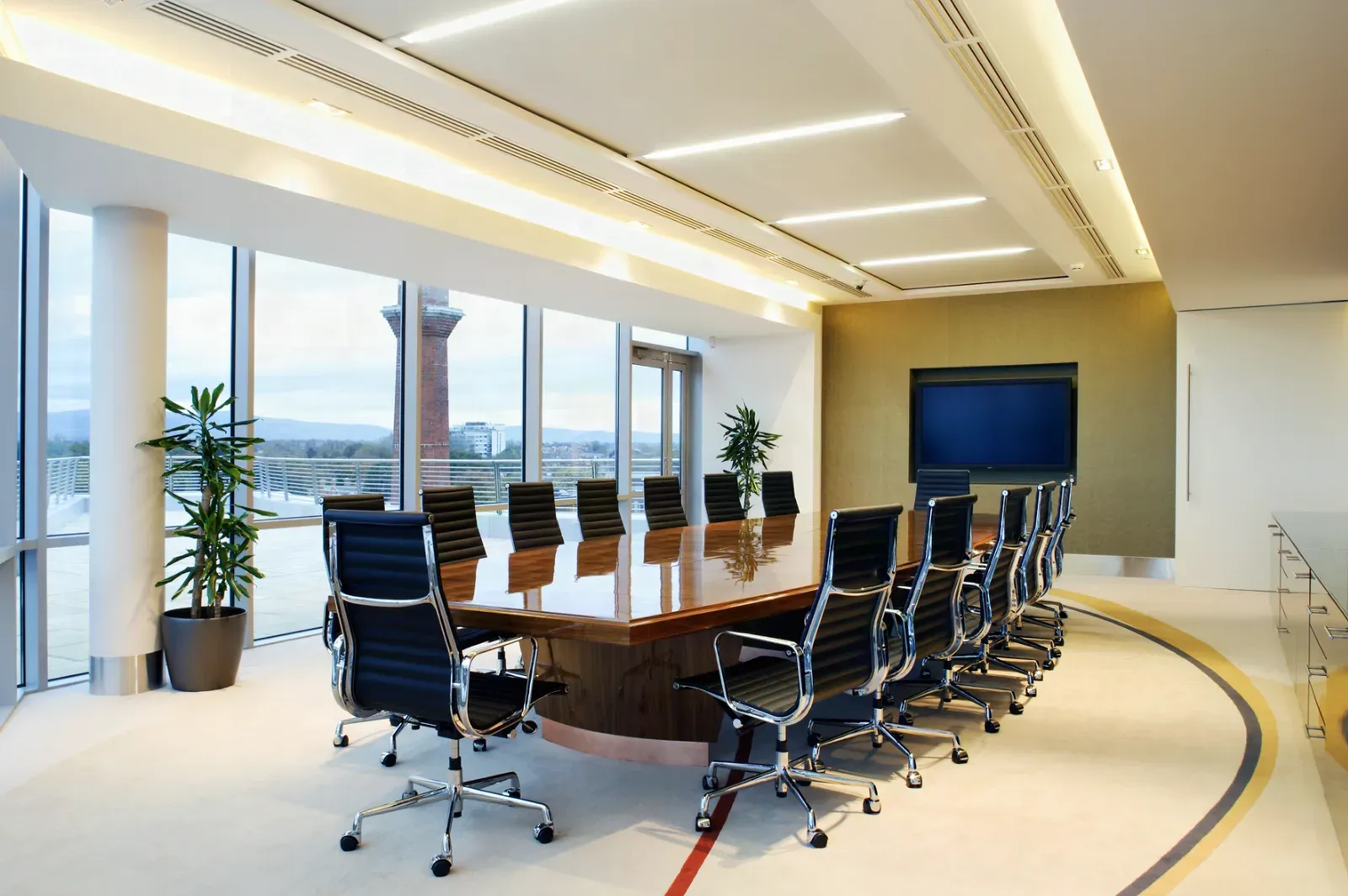 Finished corporate boardroom with a cove-lit curved drywall soffit ceiling, a long wood conference table, and a glass partition wall