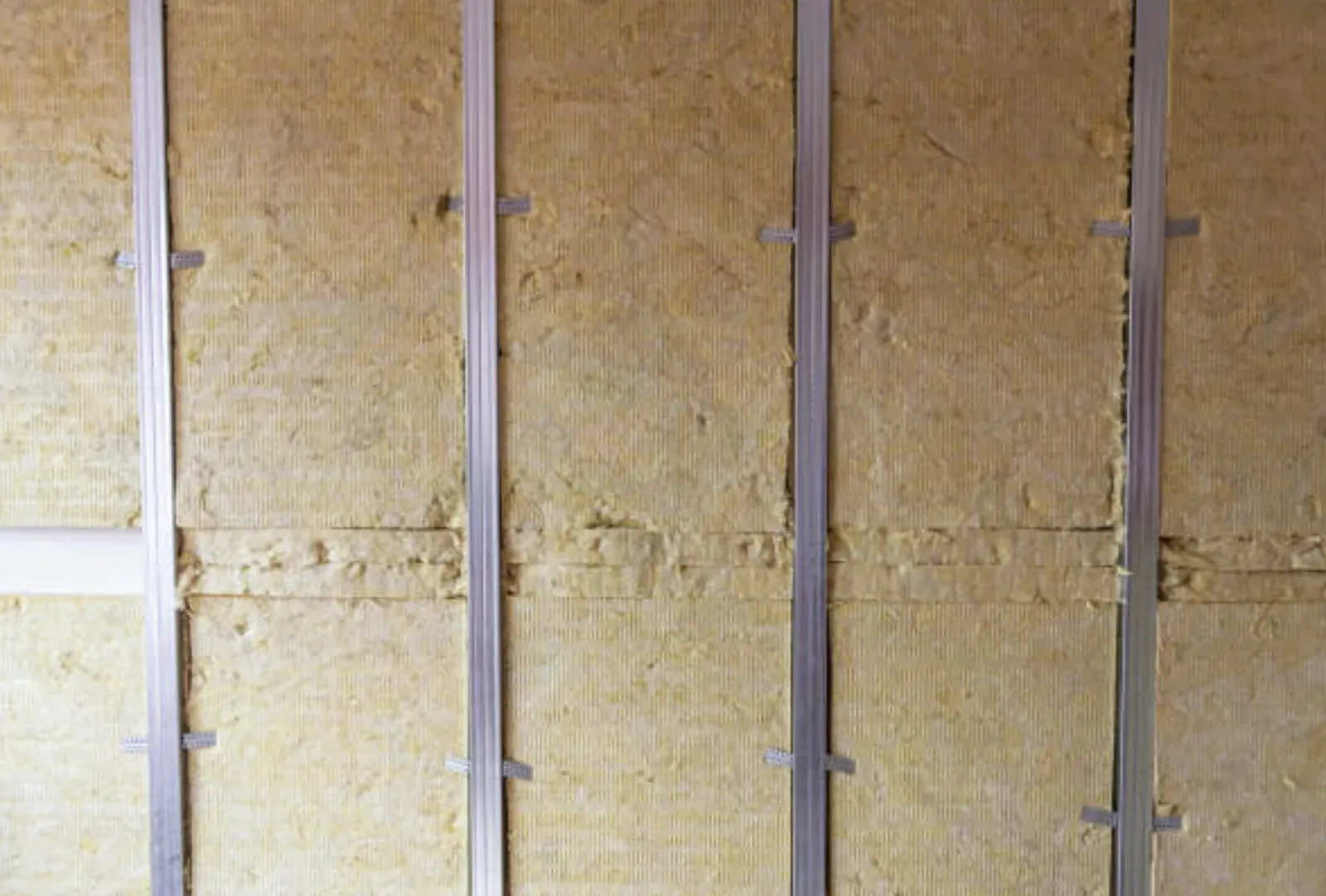 Mineral-wool sound insulation batts fitted between vertical steel studs in a partition wall, ready for drywall